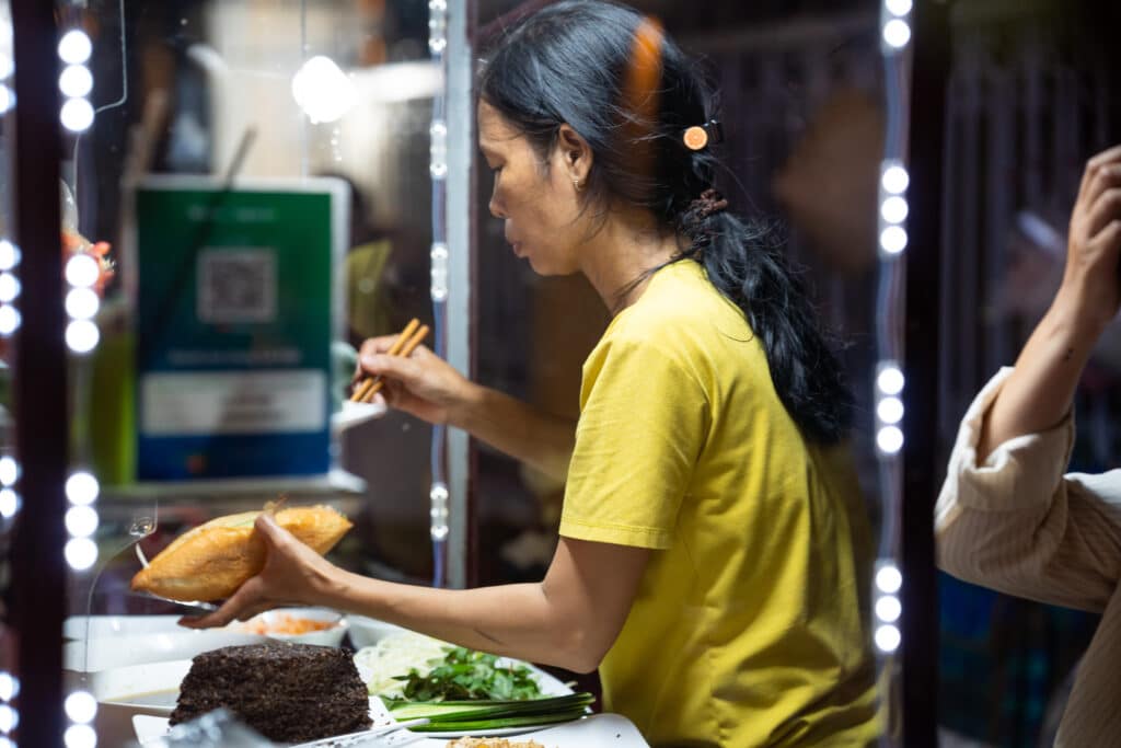 image from Hoi Banh My Chay local banh mi food stall  in hoi an vietnam featuring chef preparing a banh mi sandwich