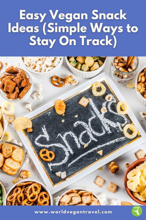 A flat-lay image of bowls filled with different vegan snacks like popcorn, pretzels, and crackers surrounding a chalkboard that says “Snacks.”