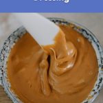 A bowl of creamy peanut dressing being stirred with a spoon.