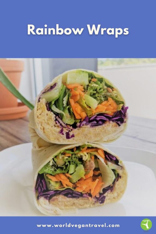 Colorful vegan rainbow wraps filled with cabbage, carrots, lettuce, and chickpeas, sliced in half on a plate.