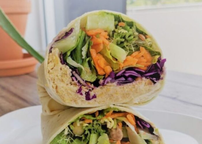 Colorful vegan rainbow wraps filled with cabbage, carrots, lettuce, and chickpeas, sliced in half on a plate.