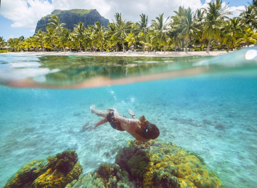 Diving teenage boy snorkeling over the coral reefs underwater photo in the clean turquoise lagoon on Le Morne palm trees beach with Le Morne Brabant mount. Mauritius island. Exotic traveling concept.