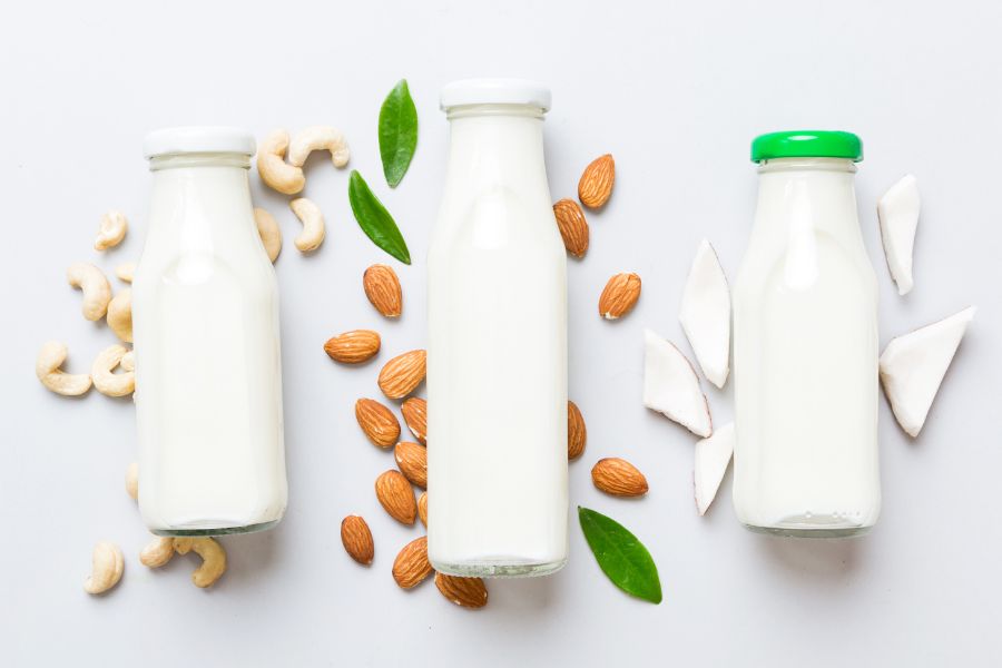 Three bottles of plant-based milk surrounded by almonds, cashews, and coconut pieces.