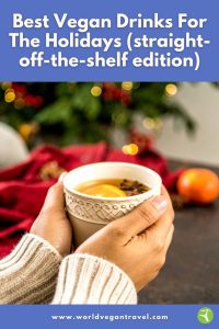 Hands holding a warm cup of vegan holiday drink with slices of orange and star anise, in front of a festive Christmas background.