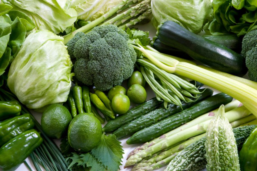 Variety of fresh green vegetables including lettuce, broccoli, cucumbers, asparagus, and zucchinis, World Vegan Travel.