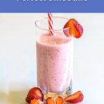 A tall pink vegan smoothie in a clear glass with fresh strawberries around it, styled for a World Vegan Travel blog post about how to make the perfect smoothie.