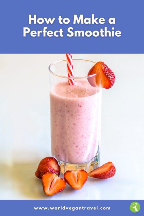 A tall pink vegan smoothie in a clear glass with fresh strawberries around it, styled for a World Vegan Travel blog post about how to make the perfect smoothie.