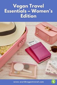 Flat lay of vegan-friendly travel essentials for women, including a pink suitcase, hat, passport, and toiletries.