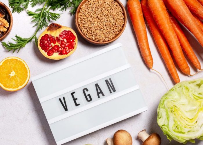 Fresh fruits, vegetables, grains, and a sign that says ‘Vegan’ displayed on a table representing the history of plant-based living.
