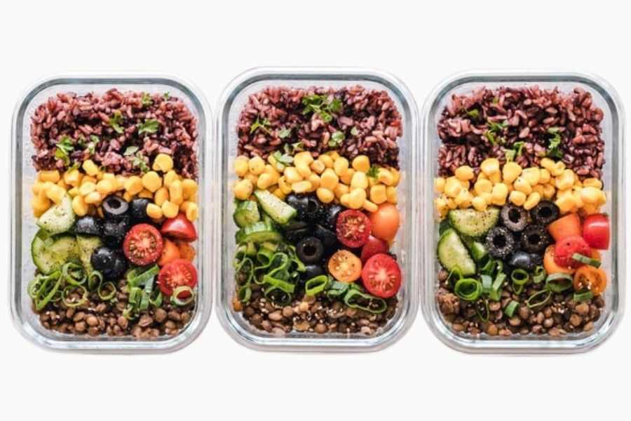 Three clear containers filled with colourful vegan meal prep bowls made with grains, veggies, and beans.