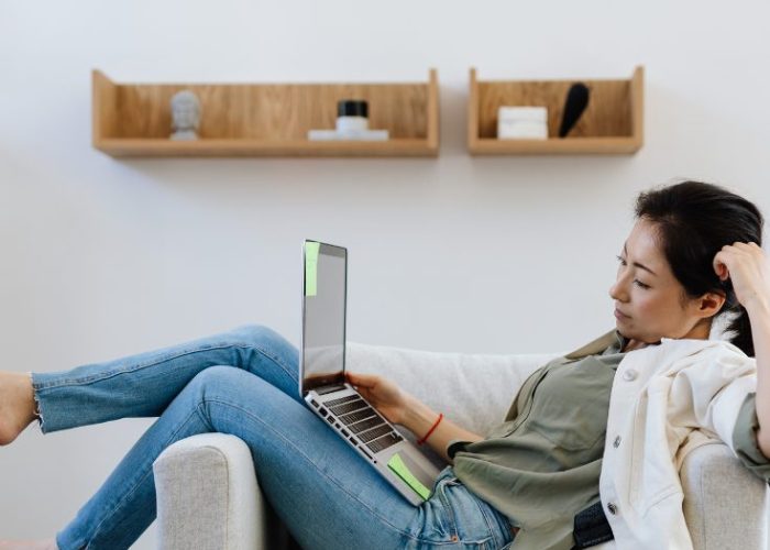 A woman relaxing in an armchair while exploring travel ideas on her laptop, showing how armchair travel lets you explore the world from home.