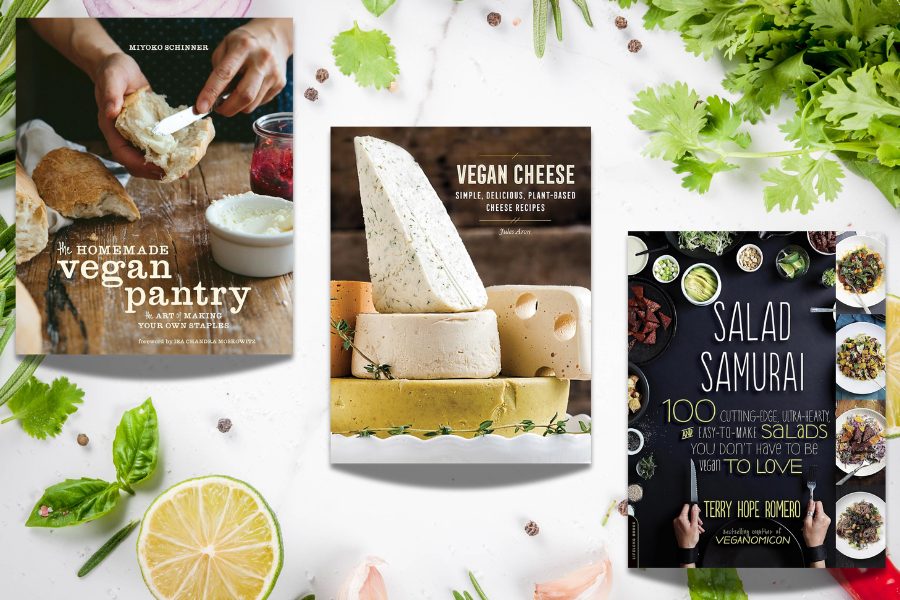 Three vegan cookbooks — The Homemade Vegan Pantry, Vegan Cheese, and Salad Samurai — displayed with fresh herbs and veggies on a bright kitchen background.