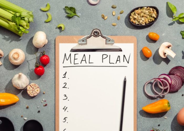 Clipboard with a meal plan surrounded by fresh vegetables and ingredients on a kitchen counter.