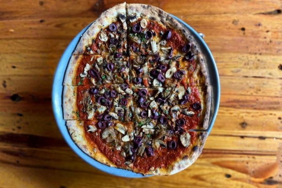 Vegan wood-fired pizza topped with olives and vegetables at Creekbread in Whistler.