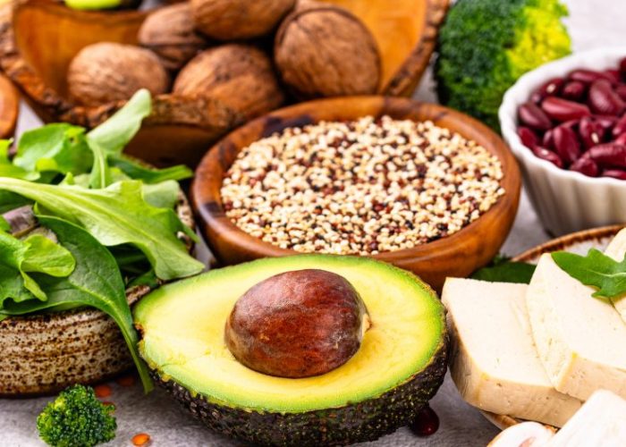 A colorful display of vegan breakfast ingredients including avocado, tofu, greens, mushrooms, quinoa, and nuts.