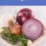 A plate with fresh garlic, red onion, shallots, and herbs displayed on a wooden table.