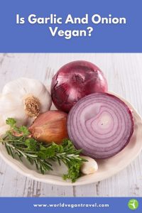 A plate with fresh garlic, red onion, shallots, and herbs displayed on a wooden table.