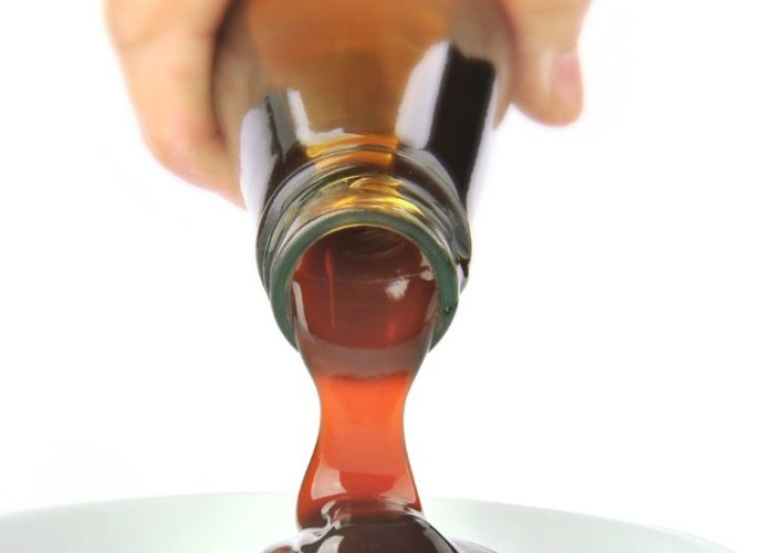 A bottle of dark oyster sauce being poured into a white dish, showing the thick glossy texture.