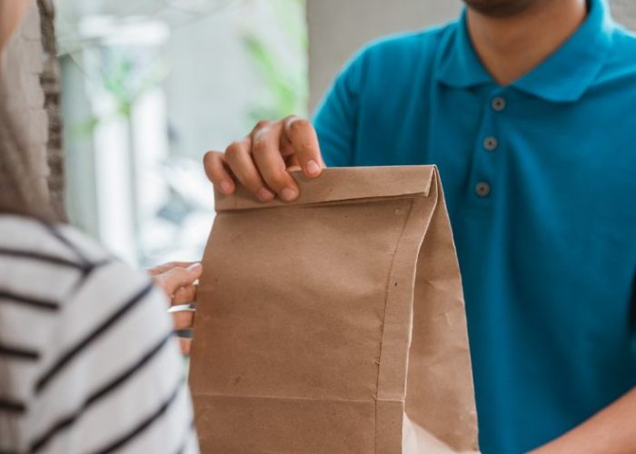 Person receiving a plant-based meal delivery bag at their door, representing the PlantX vegan meal delivery service, featured by World Vegan Travel.