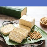 Fresh slices of tempeh on a banana leaf board, ready to cook, for the Tempeh for Beginners guide on World Vegan Travel.