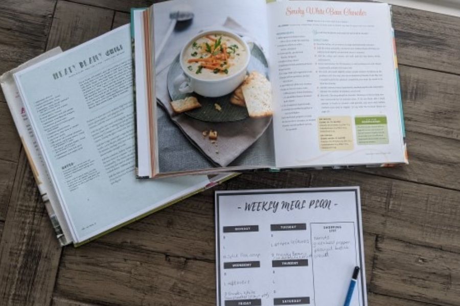 Open vegan cookbooks and a weekly meal planning sheet with a pen on a wooden table.