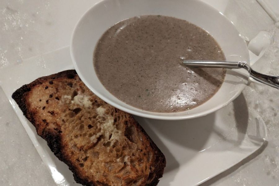 A warm bowl of creamy vegan mushroom soup served with toasted sourdough bread.