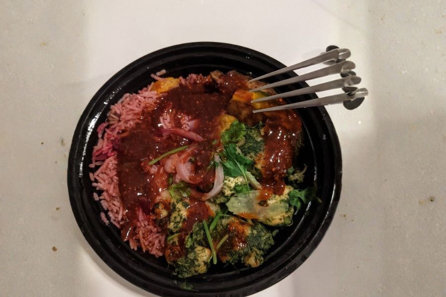A colorful vegan squash masala meal with beet rice, greens, and flavorful sauce in a black bowl.