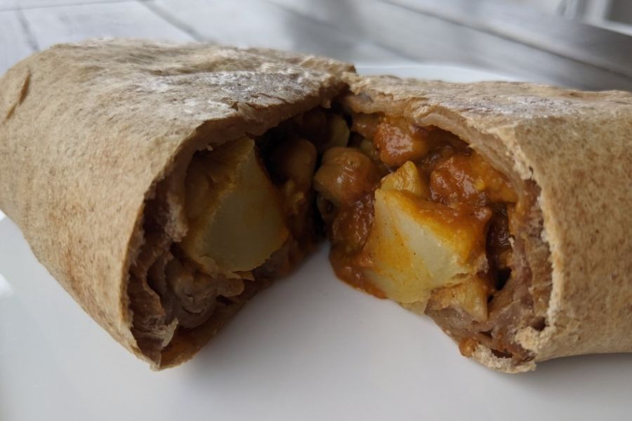 A vegan Bombay chickpea wrap cut open to show potatoes, chickpeas, and spicy tomato filling.