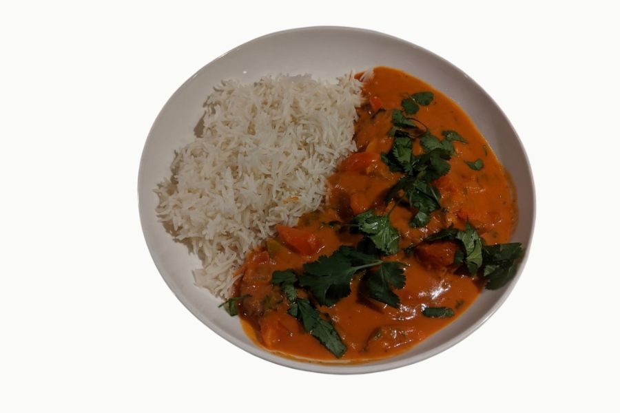 A bowl of creamy orange tempeh curry served with white rice and fresh herbs.