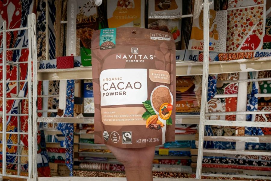 A bag of Navitas Organic Cacao Powder held up in a store filled with colorful products.