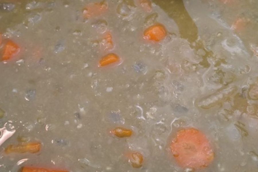 Close-up of vegan split pea soup cooking with carrots and peas.