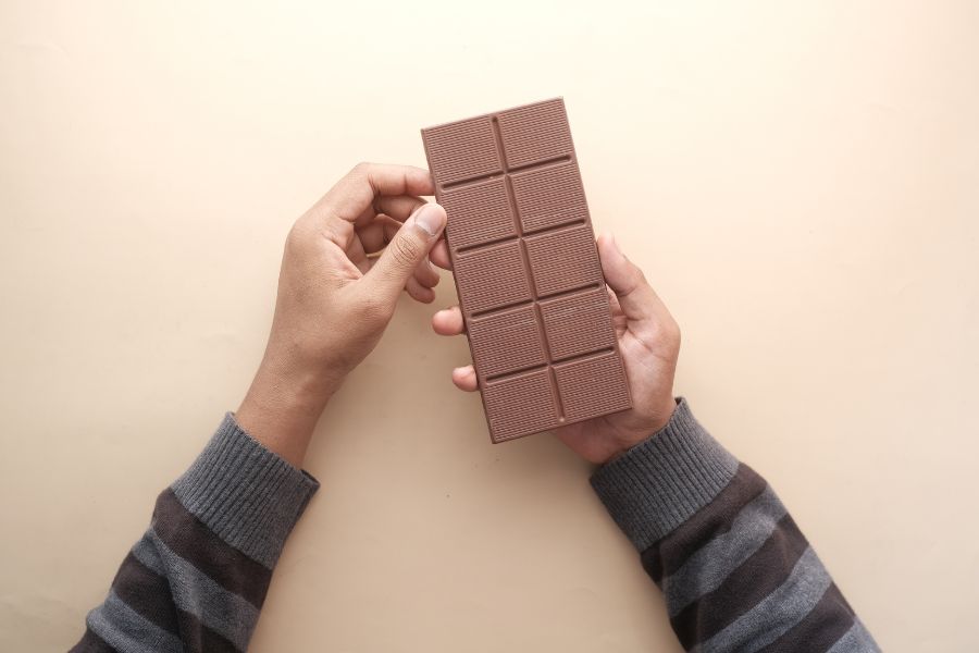 Person holding a plain chocolate bar with both hands over a beige background.