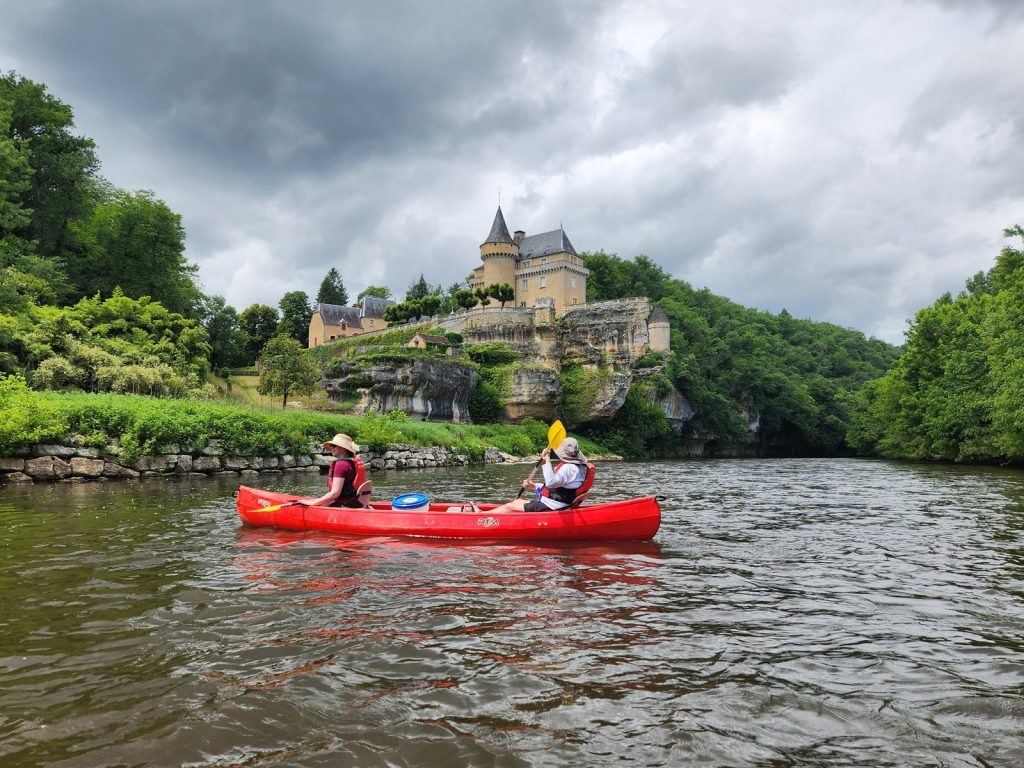 Two people canoeing past a castle on the river in Dordogne, France