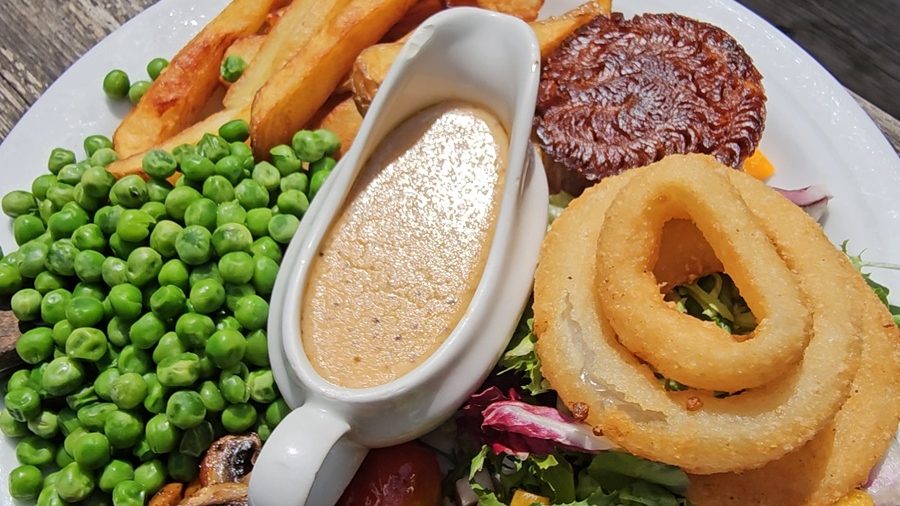 Plate of vegan comfort food with fries, peas, mushrooms, salad, onion rings, and gravy