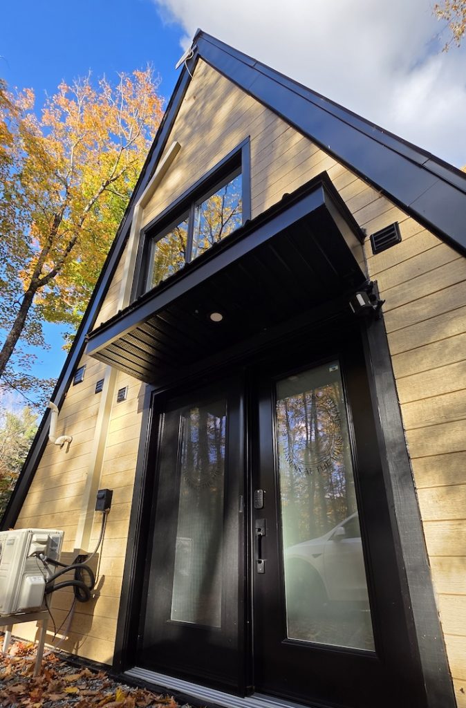 Modern A-frame cabin with tall windows surrounded by golden autumn leaves in Quebec.