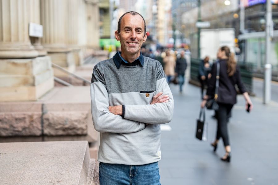 Dr Lee Hawkins standing on a Melbourne street, smiling with people walking in the background.