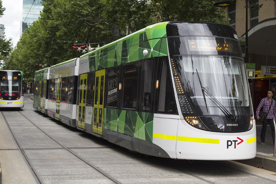 Modern green trams traveling along a tree-lined street in central Melbourne, Australia.
