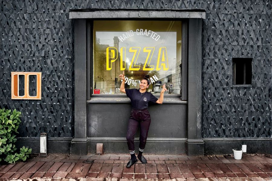 Carla standing outside a vegan pizza shop in London, smiling and pointing at the window