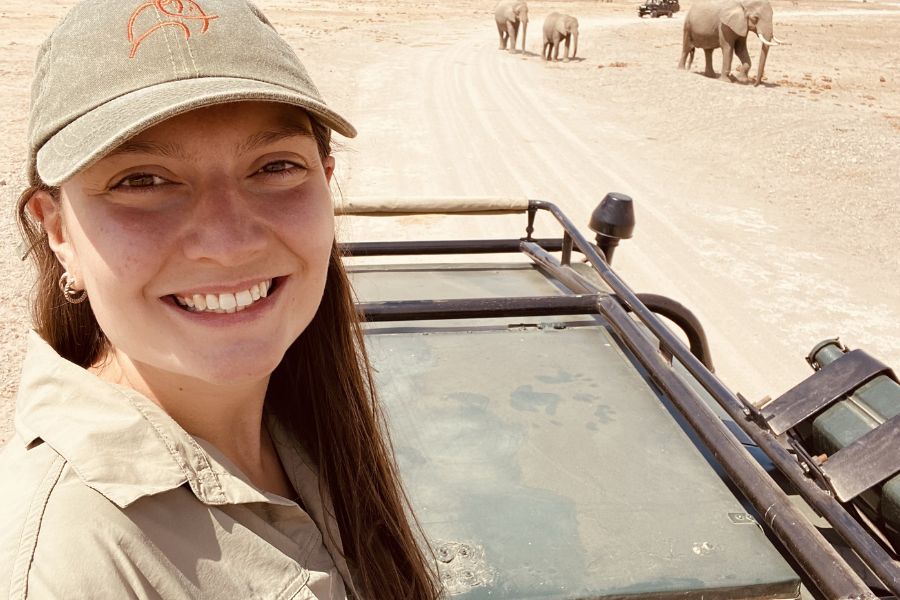 Dr Katie Thompson smiling on safari with elephants in the background in South Africa.