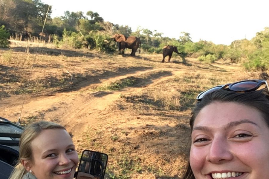 Two people smiling on safari with elephants in the background in South Africa.