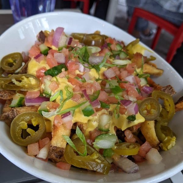 a plate of home cut fries with a vegan cheeses sauce and a homemade salsa with jalapenos in a bowl on a table