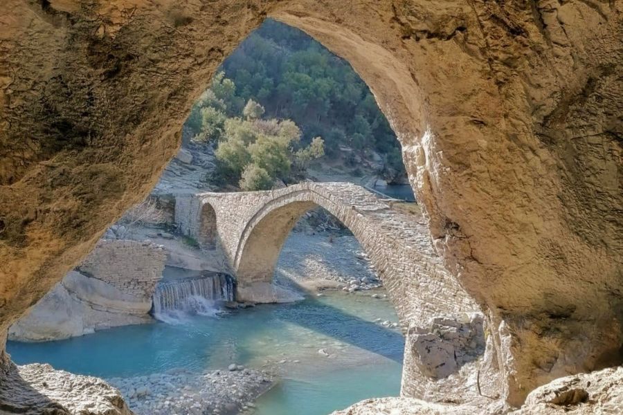 View from inside a cave in Albania looking out to a stone bridge and river below