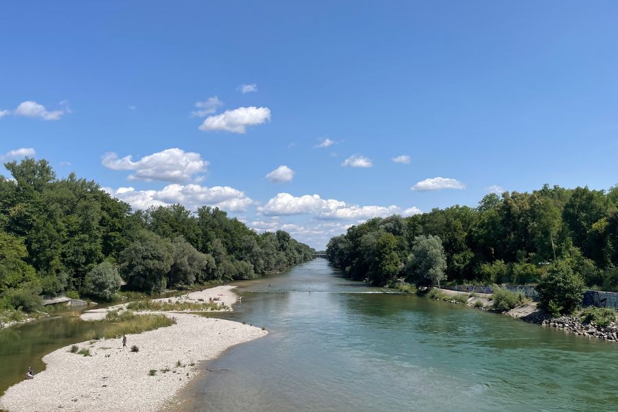 Isar River in Munich with trees, blue sky, and people relaxing by the water