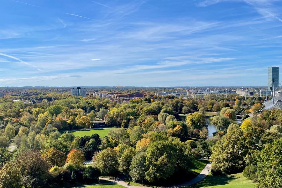 View over Olympiapark Munich with trees, blue sky, and city buildings