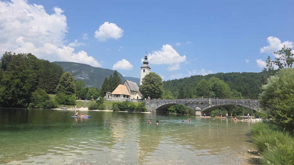 Swimmers beside the stone bridge and lakeside church at Lake Bohinj