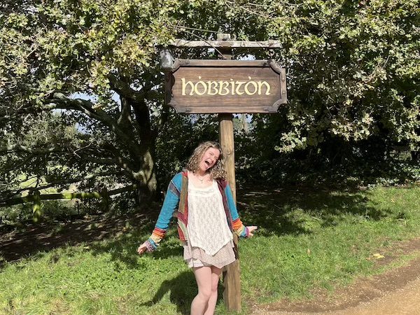 Traveler Kiara beside the Hobbiton sign during a New Zealand adventure