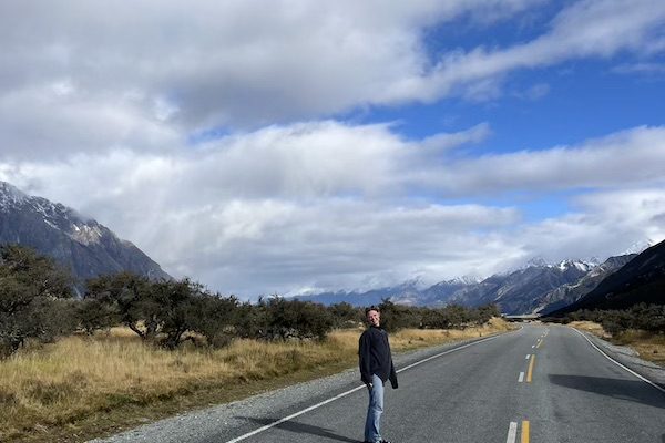 Traveler Kiara standing on a scenic road surrounded by mountains in New Zealand
