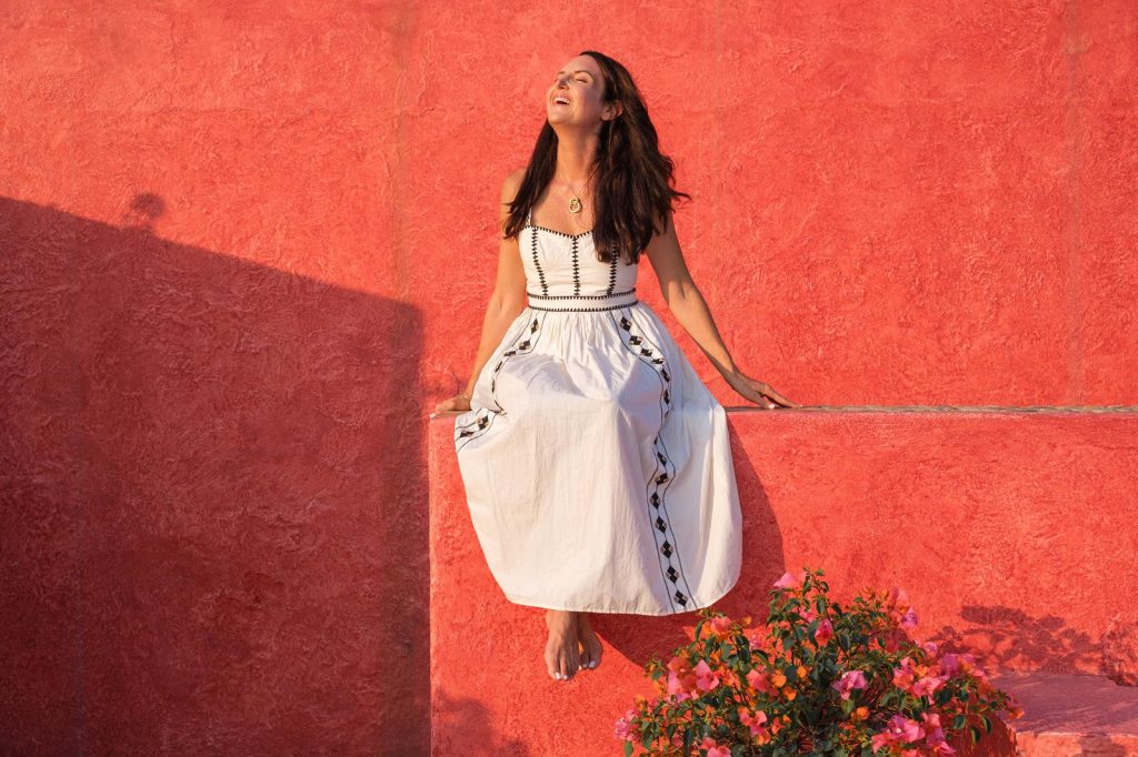 Kim Kessler smiling against a coral-red wall in Careyes, Mexico