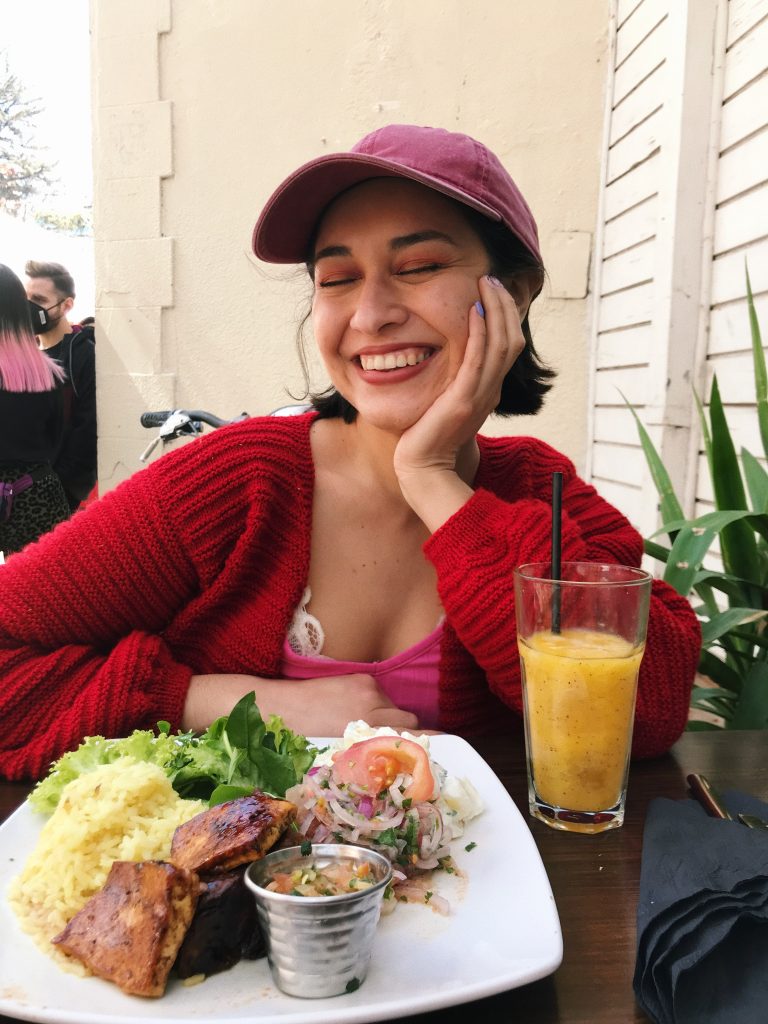 Natalia Rojas sitting at a restaurant table with a plate of rice, salad, and a yellow drink.
