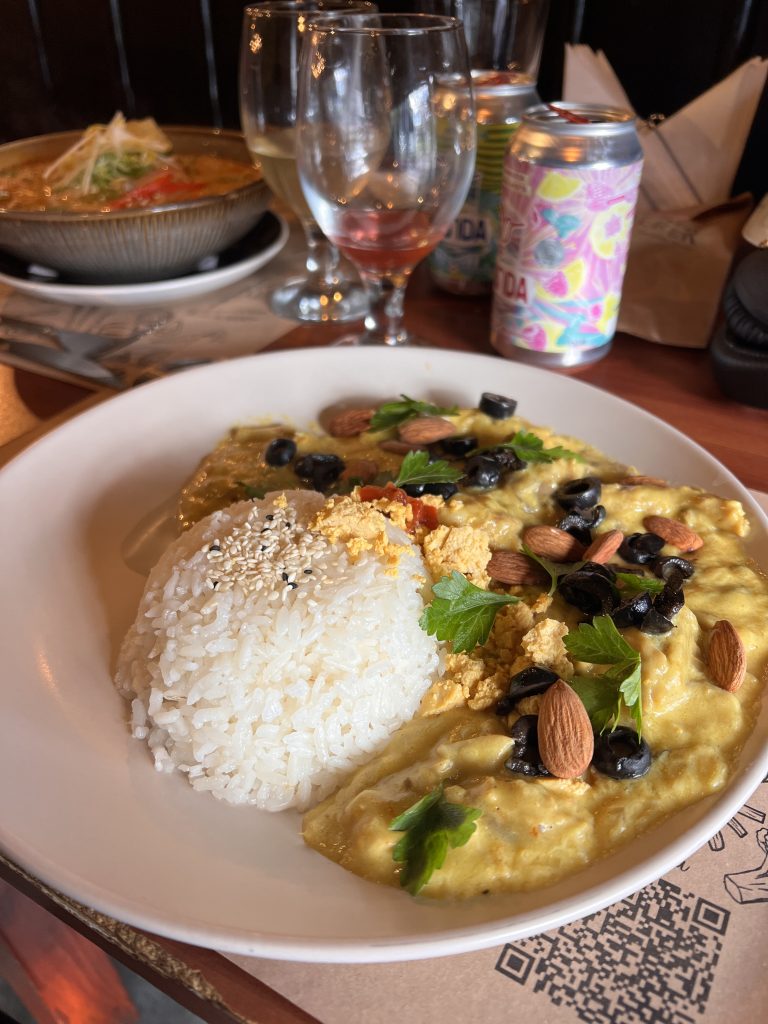 Rice beside a creamy yellow dish topped with sliced black olives, almonds, and fresh herbs.